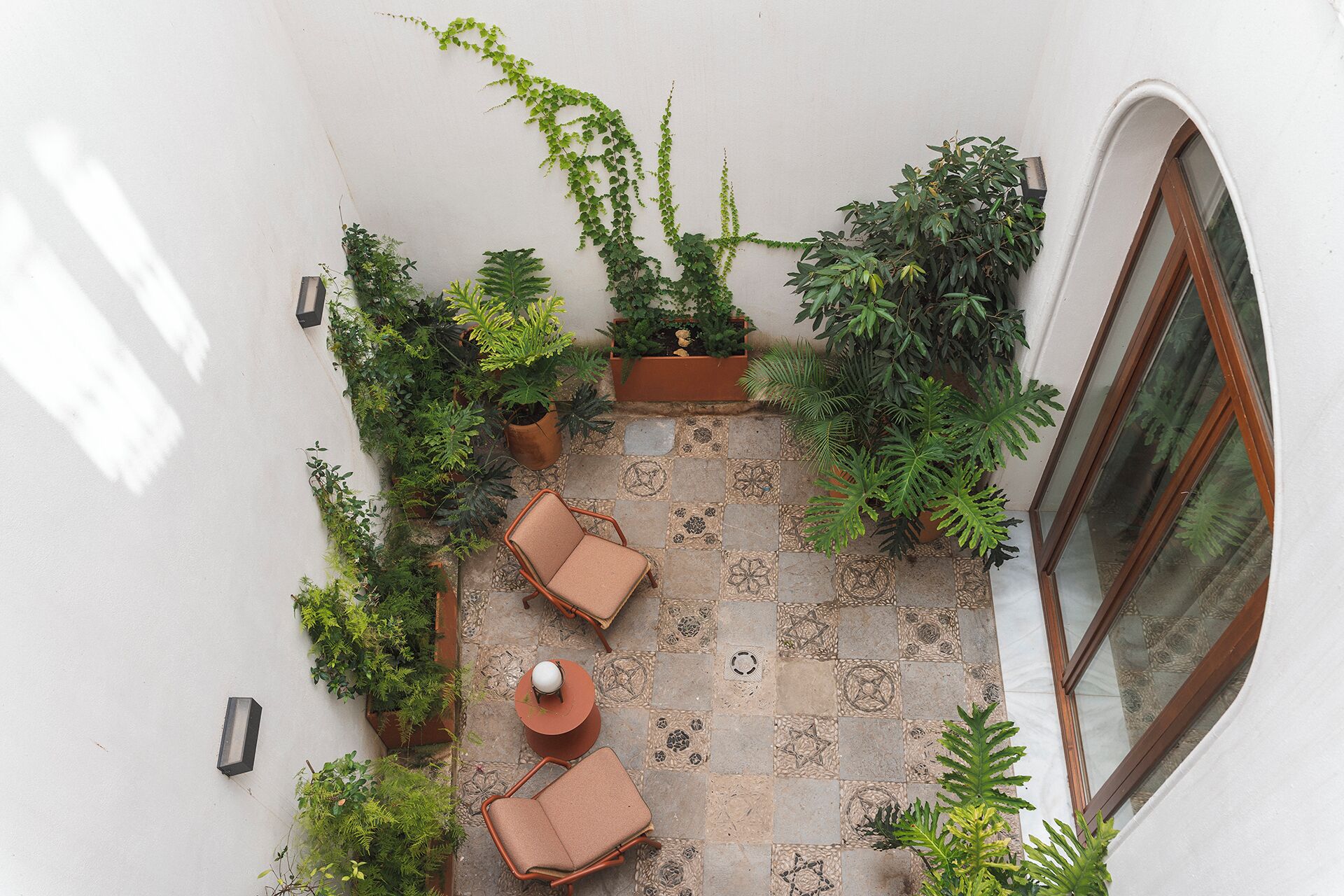 A rooftop patio with two cushioned chairs, a small table, and various potted plants.