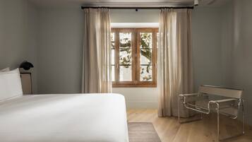 Una habitación de hotel moderna con una cama grande, un escritorio con una silla, una ventana con cortinas y vistas a árboles.
