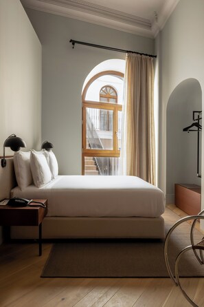 A bedroom with a bed, a nightstand, a lamp, and a view of a staircase through an arched window. - Mercer Residences Sevilla (Seville)