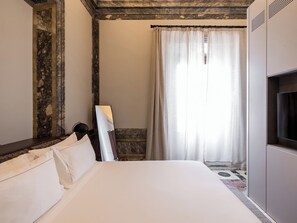 A hotel room with a bed, a TV, a window with curtains, and a stone wall. - Mercer Residences Sevilla (Seville)