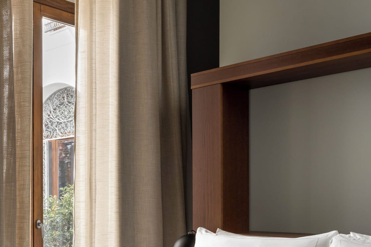 Quarto de hotel com uma cama, cabeceira de madeira e uma janela com cortinas.