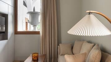 Ein modernes Wohnzimmer mit einem beigefarbenen Sofa, einem Holztisch und einer Stehlampe. Durch ein mit Vorhängen drapiertes Fenster fällt natürliches Licht ein.