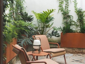 A patio with two brown chairs, a small table, and various potted plants. - Mercer Residences Sevilla (Seville)