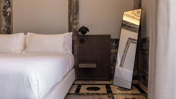 Un lit bien fait, avec du linge de lit blanc, une armoire en bois, un grand miroir doté d’un cadre décoratif et un sol à motifs.