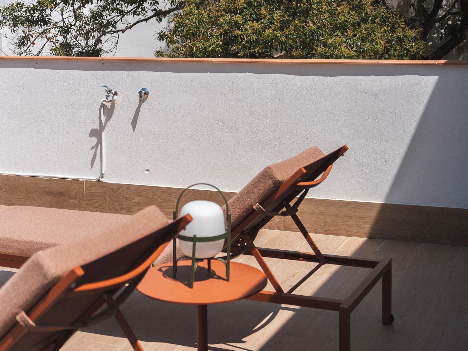 A sun lounger and a small table with a white lamp on a rooftop terrace.