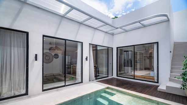 Ein moderner Poolbereich im Freien mit Glasschiebetüren zu einem Wohnbereich, einer Holzterrasse und blauem Himmel.