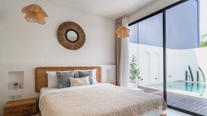 Ein Schlafzimmer mit einem großen Bett, einem runden Spiegel und Blick auf einen Swimmingpool.