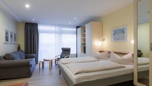 Quarto de hotel moderno com cama, sofá, poltrona e uma pequena mesa.