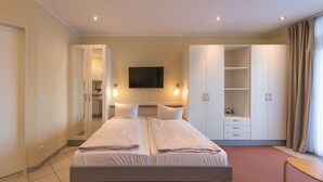 A modern bedroom with a double bed, a TV mounted on the wall, and a wardrobe with multiple compartments. - Ferienwohnung im Aparthotel Seepanorama (Granzow)