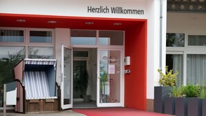 A building entrance with a red awning and a sign that reads "Herzlich Willkommen". - Ferienwohnung im Aparthotel Seepanorama (Granzow)