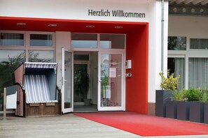 L'ingresso di un edificio con tenda rossa e insegna con la scritta "Herzlich Willkommen".