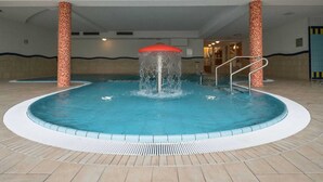 An indoor swimming pool with a central water feature, surrounded by tiled flooring and columns with patterned bases. - Ferienwohnung im Aparthotel Seepanorama (Granzow)
