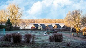 A row of traditional-style cottages with sloped roofs, a grassy yard, and a forested hill in the background. - Ferienwohnung im Aparthotel Seepanorama (Granzow)