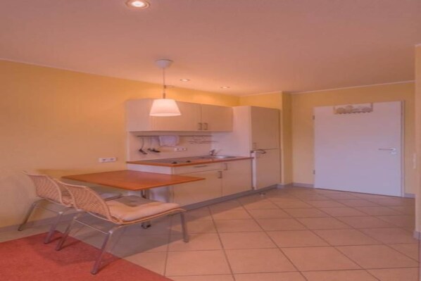 Une cuisine compacte avec un coin repas, comprenant une petite table, des chaises et un luminaire suspendu.