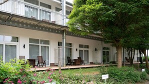 A hotel with a covered outdoor seating area, a garden with flowering plants, and a tree. - Apartment für den perfekten Urlaub (Granzow)