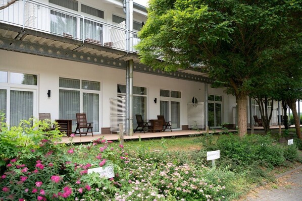Un hôtel doté d’un espace extérieur couvert avec des sièges, d’un jardin agrémenté de plantes fleuries et d’un arbre.