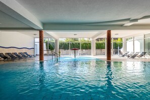 Ein Hallenbad mit klarem Wasser, umgeben von Liegestühlen und einer Glaswand.