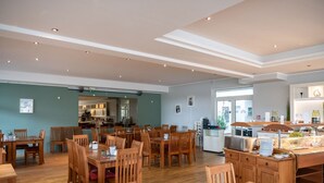 Un comedor amplio con mesas y sillas de madera, un mostrador de buffet y una cocina al fondo.