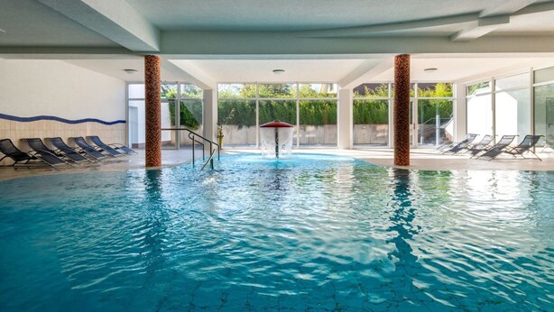 Una piscina interior con agua cristalina, rodeada de sillones de descanso y un muro de vidrio.