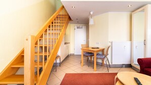 Un espace de vie compact doté d’un escalier en bois, d’un coin repas avec une table et des chaises, d’un canapé rouge et d’un tapis rouge.