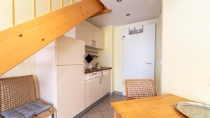 Une cuisine compacte avec un escalier en bois, un coin repas avec une table et des chaises, et une porte blanche dotée d’une petite fenêtre.