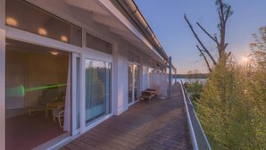 A covered outdoor area with a wooden deck, glass doors leading to a room, and a view of the surrounding landscape. - Elegant eingerichtete Ferienwohnung (Granzow)