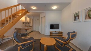 A modern living room with a wooden staircase, a flat-screen TV, and a dining area with two chairs and a table. - Elegant eingerichtete Ferienwohnung (Granzow)