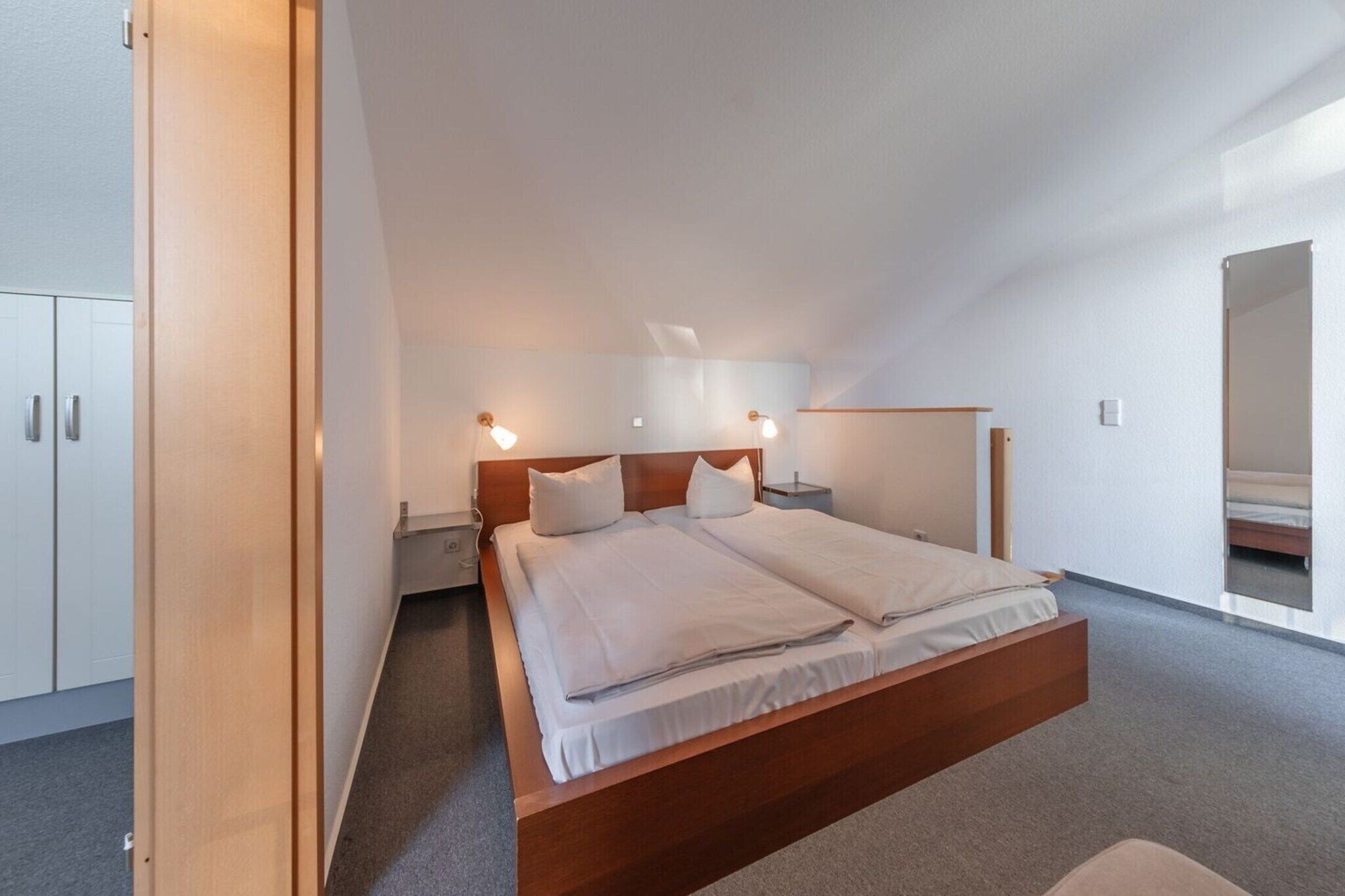 A modern bedroom with a large bed, bedside tables, and a wardrobe.