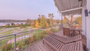 A wooden deck with outdoor seating, overlooking a parking area and a body of water with buildings in the distance. - elegant eingerichtete Ferienwohnung (Granzow)