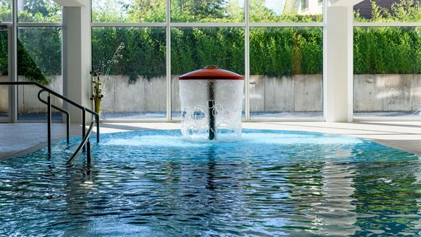 A swimming pool with a water fountain, surrounded by large windows and a concrete wall. - elegant eingerichtete Ferienwohnung (Granzow)