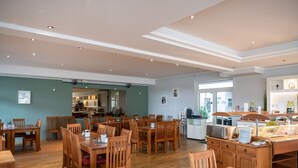 Uma ampla área de refeições com mesas e cadeiras de madeira, um buffet e uma cozinha ao fundo.