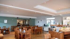 A spacious dining area with wooden tables and chairs, a buffet station, and a kitchen in the background. - elegant eingerichtete Ferienwohnung (Granzow)