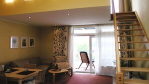 A living room with a sofa, chairs, a table, a staircase, and a view through a glass door. - elegant eingerichtete Ferienwohnung (Granzow)