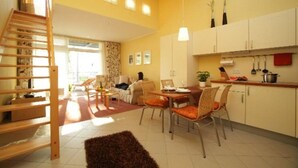 Amplia sala de estar con mesa de comedor, sillas, una escalera y zona de cocina con alacenas y un colgador para ollas.