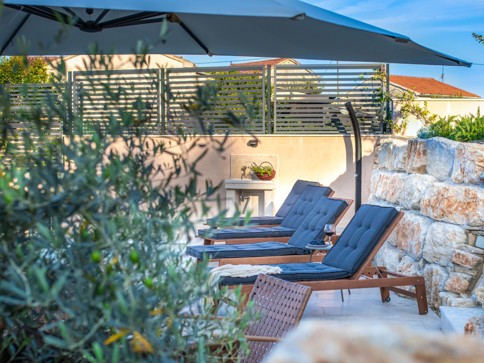 Een zonnig terras met lounge stoelen en een tafel, omgeven door stenen muren en beplanting.