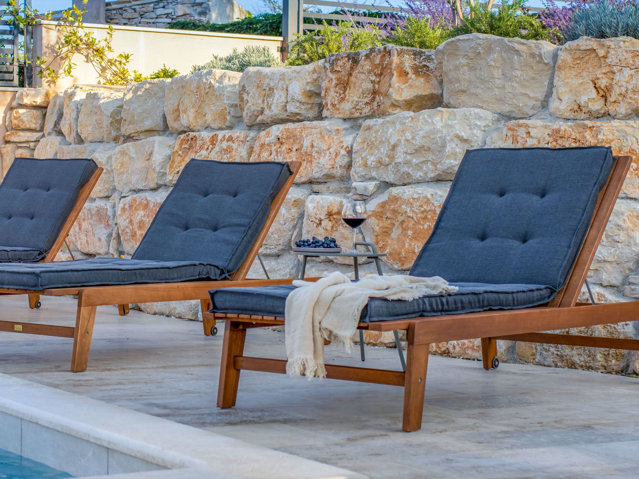 A poolside area with three lounge chairs and a table with a glass of wine and blueberries.