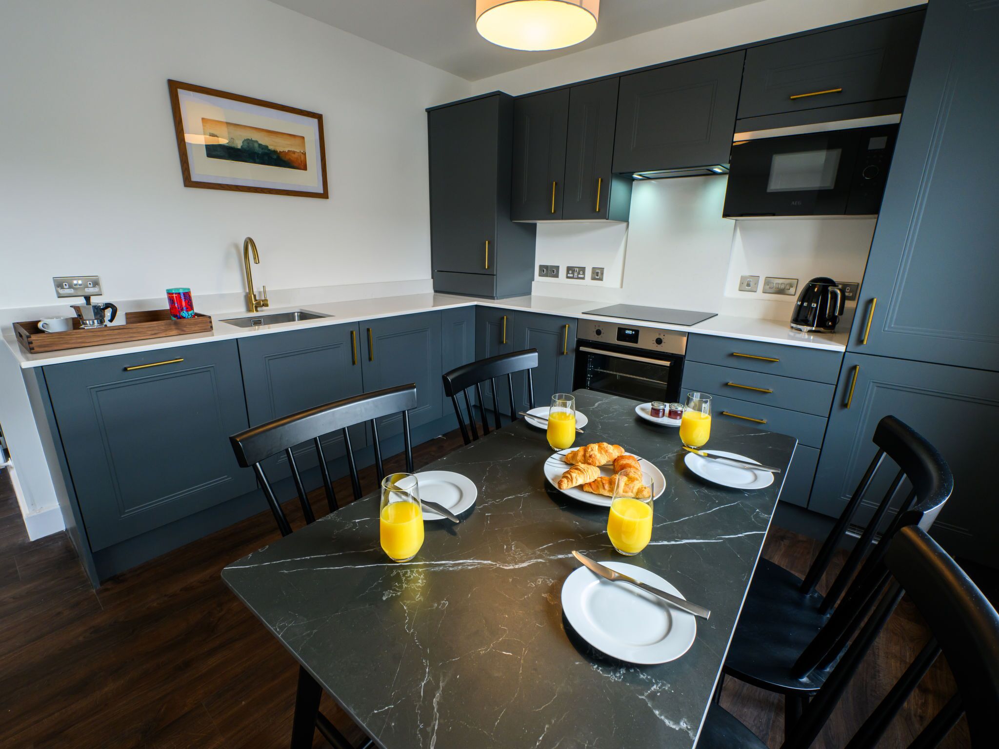 Una cocina moderna con armarios azul oscuro, encimera de mármol y una mesa de desayuno servida.