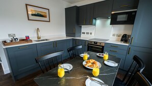 Cozinha moderna com armários azul escuro, bancada de mármore e mesa de jantar posta para o café da manhã.