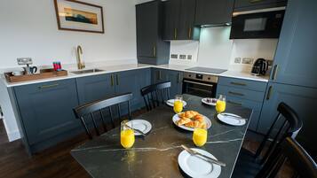 Une cuisine moderne avec des meubles de couleur bleu foncé, un plan de travail en marbre et une table à manger dressée pour le petit-déjeuner.