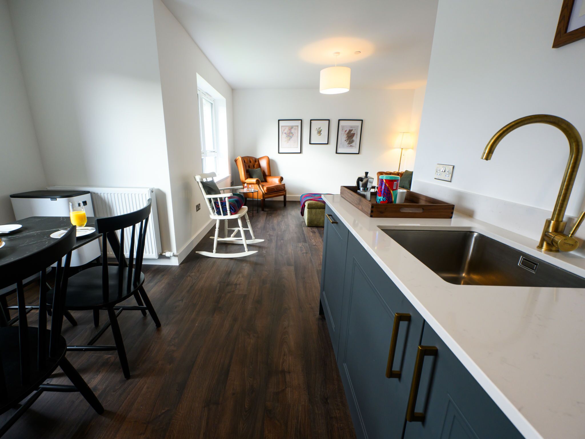 Una cocina moderna con encimera blanca, un lavamanos de acero inoxidable y una mesa de comedor de madera con sillas.