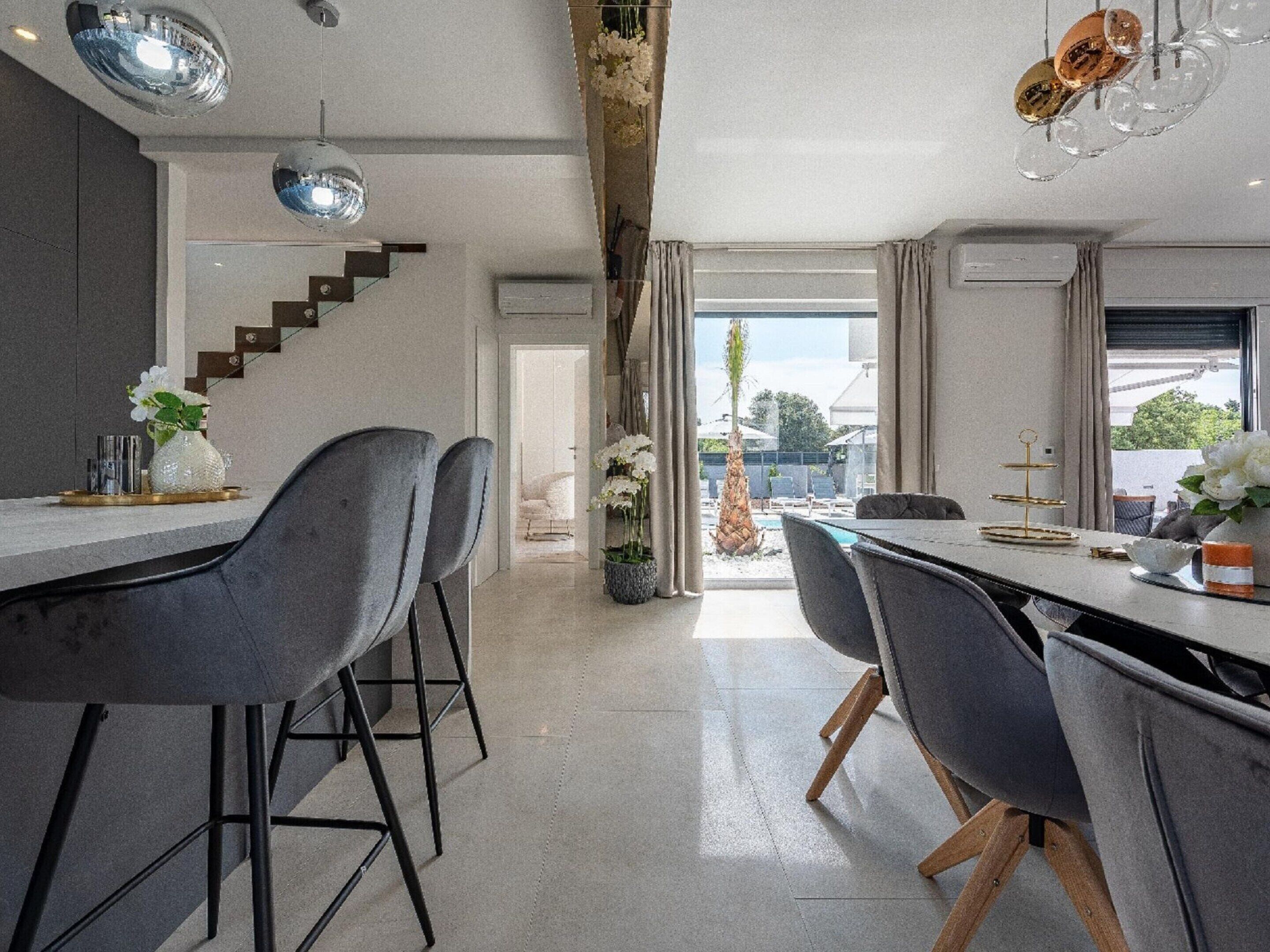 A modern kitchen with a central island, grey bar stools, and a view of the outdoors.