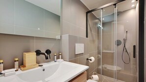 A modern bathroom with a large sink, a glass shower enclosure, and toiletries on the counter.