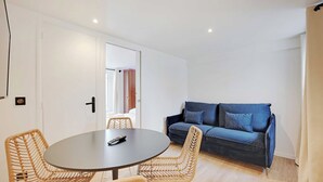A room with a round table, two wicker chairs, a blue sofa, and a door leading to another room.