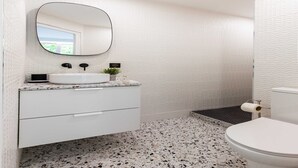 A bathroom with a white vanity, a round mirror, a sink, and a toilet.