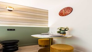 A dining area with a round table, two gold stools, a wall clock, and a patterned wall. - Cosy Studio - Parc des expositions / Tour Eiffel 11 (Paris)