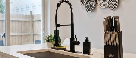 A kitchen with a sink, a faucet, a knife block, and decorative plates on the wall.