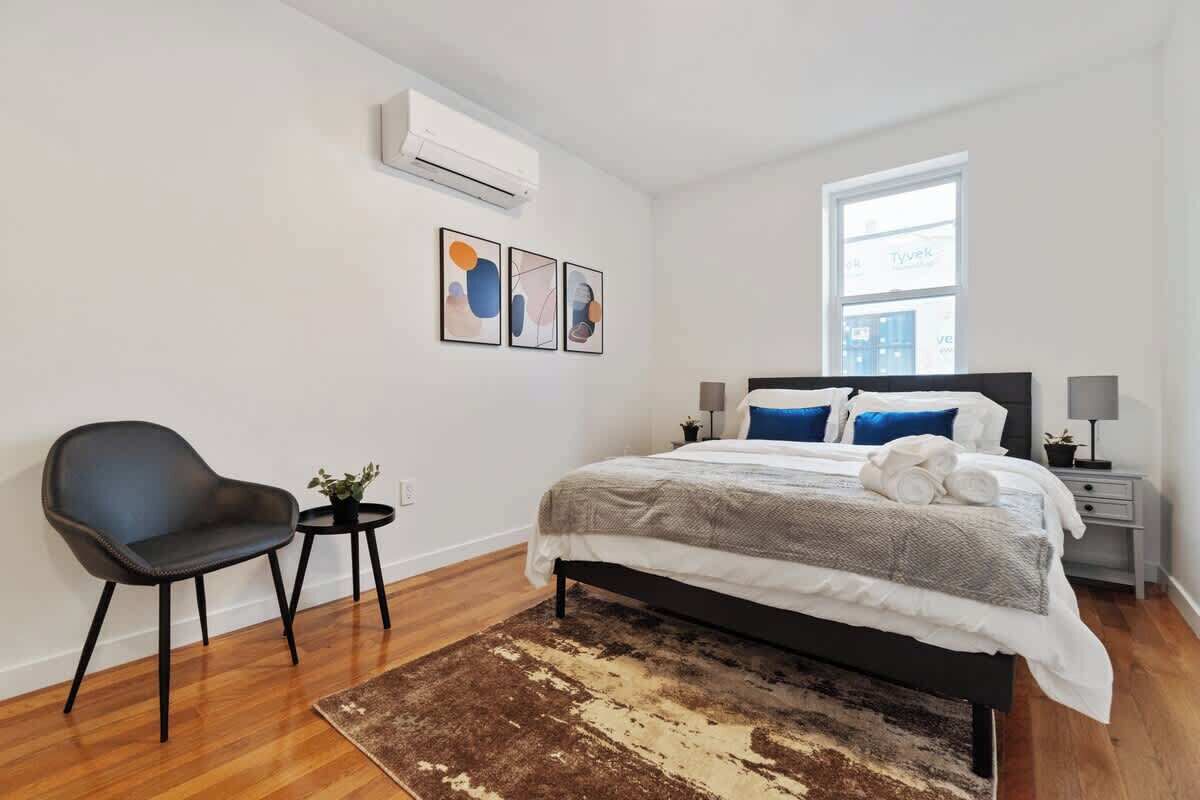 Un dormitorio moderno con una cama, una silla, una mesita y una alfombra.