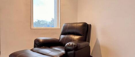 A corner room with a leather recliner chair, a window, and a wooden floor.
