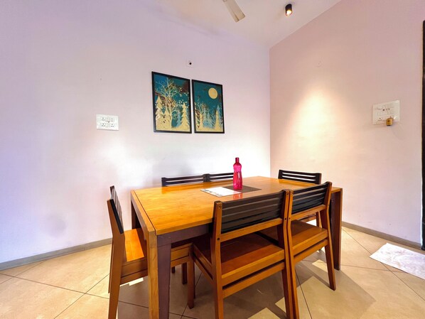 A dining area with a wooden table and chairs, two wall-mounted paintings, and a red water bottle on the table.
