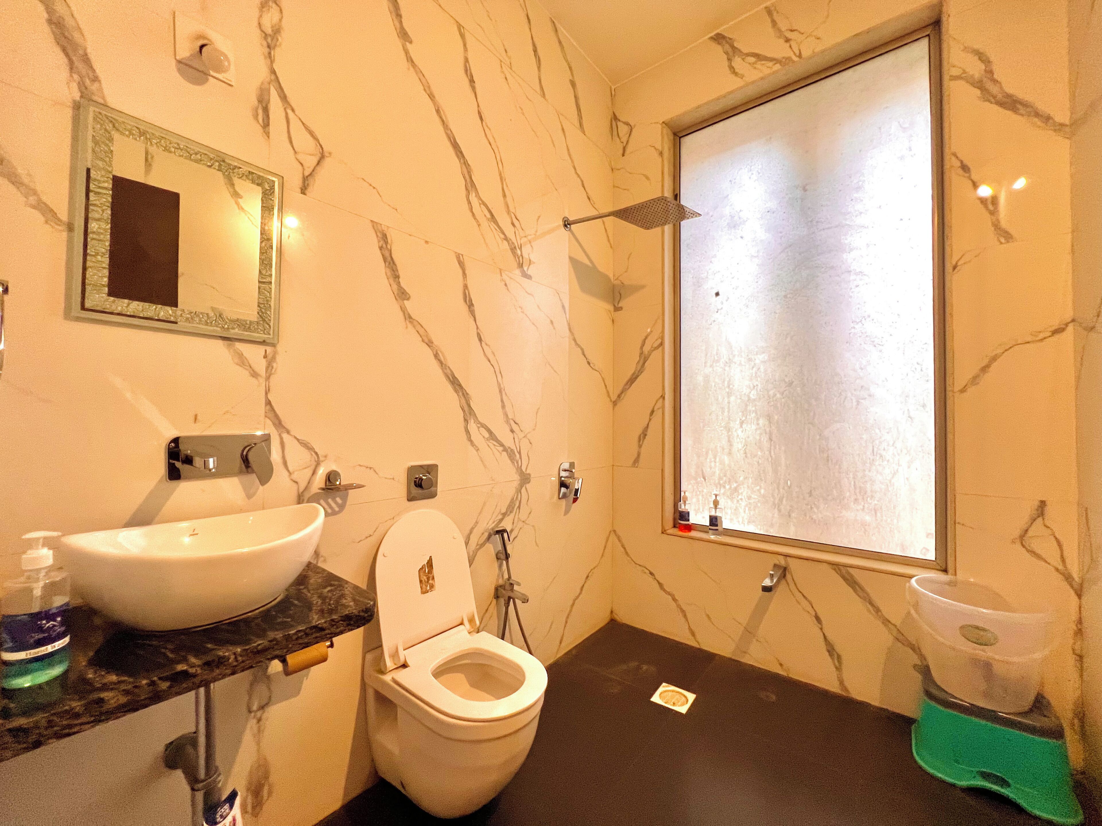 A bathroom with a marble wall, a sink, a toilet, and a window.